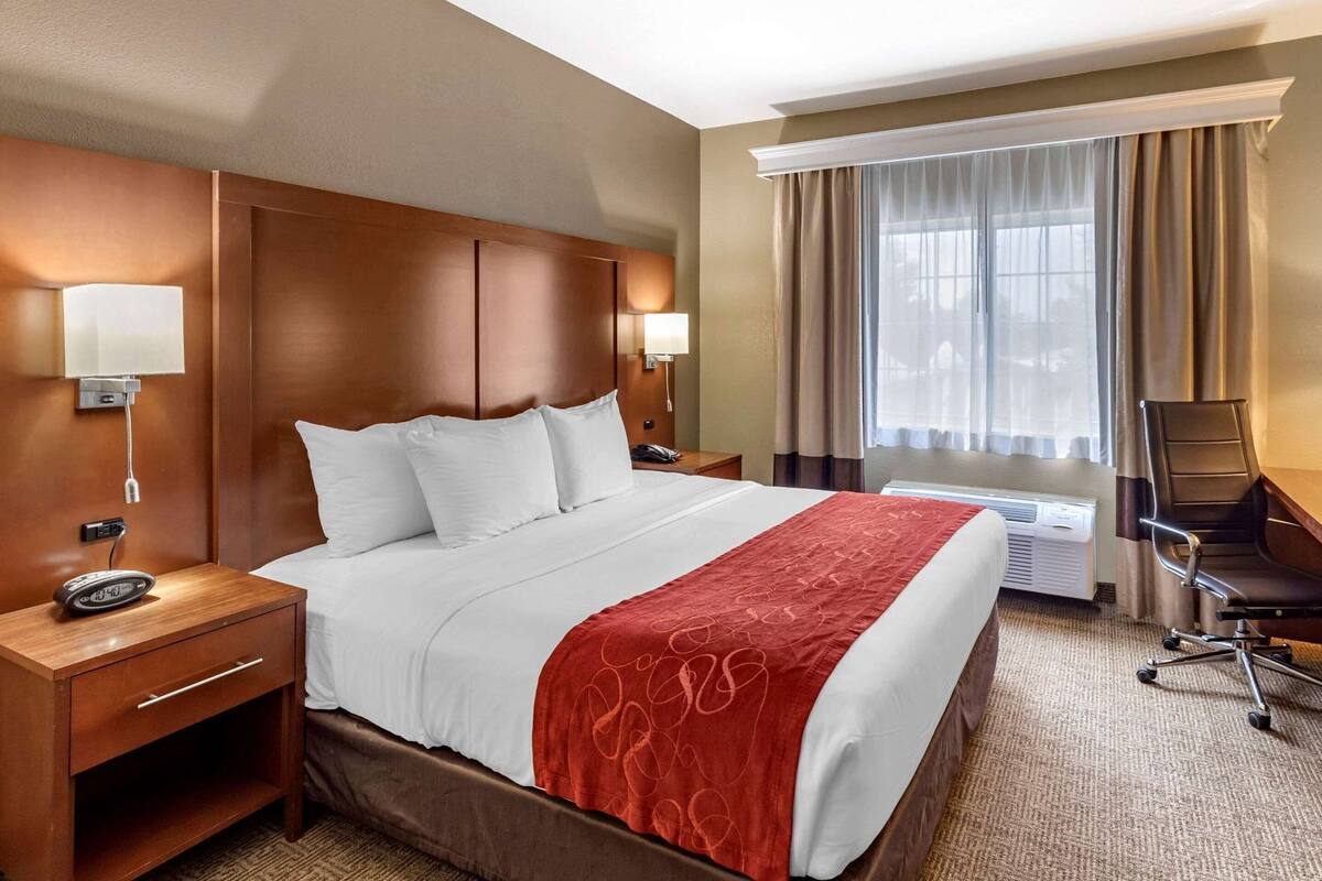 A hotel room with a large bed, bedside tables, a desk, a chair, and a window with curtains.