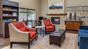 A hotel lobby with a fireplace, two armchairs, a sofa, a small table, and a kitchenette area. - Comfort Suites Fort Collins Near University (Fort Collins)