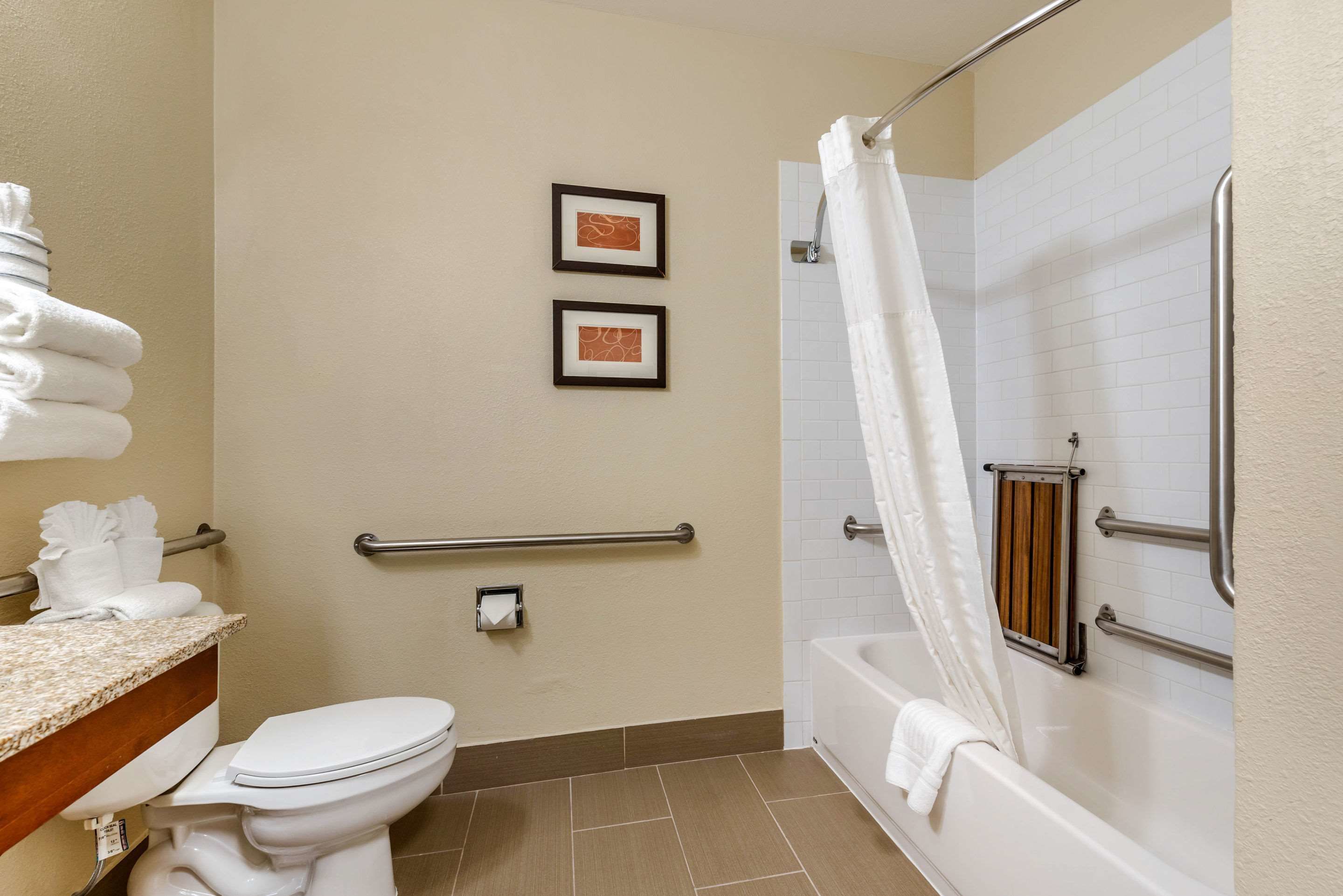 Une salle de bain avec des toilettes, un lavabo et une baignoire. Il y a deux tableaux encadrés au mur, un porte-serviettes et un rideau de douche.