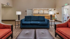 A hotel lobby with a blue sofa, red armchairs, a coffee station, and a clock on the wall. - Comfort Suites Fort Collins Near University (Fort Collins)