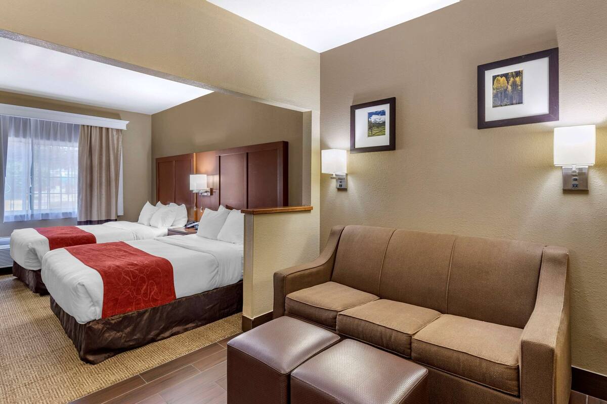 A hotel room with two beds, a sofa, a coffee table, and a desk.