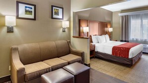 A hotel room with a brown sofa, a bed with a red blanket, and two framed pictures on the wall. - Comfort Suites Fort Collins Near University (Fort Collins)