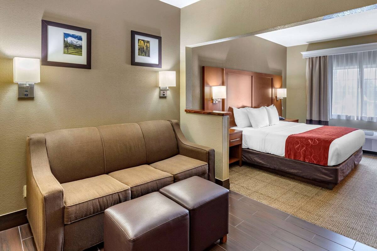 A hotel room with a brown sofa, a bed with a red blanket, and two framed pictures on the wall.