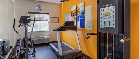 A gym with a treadmill, elliptical, and weight machine, with a clock and motivational posters on the wall.