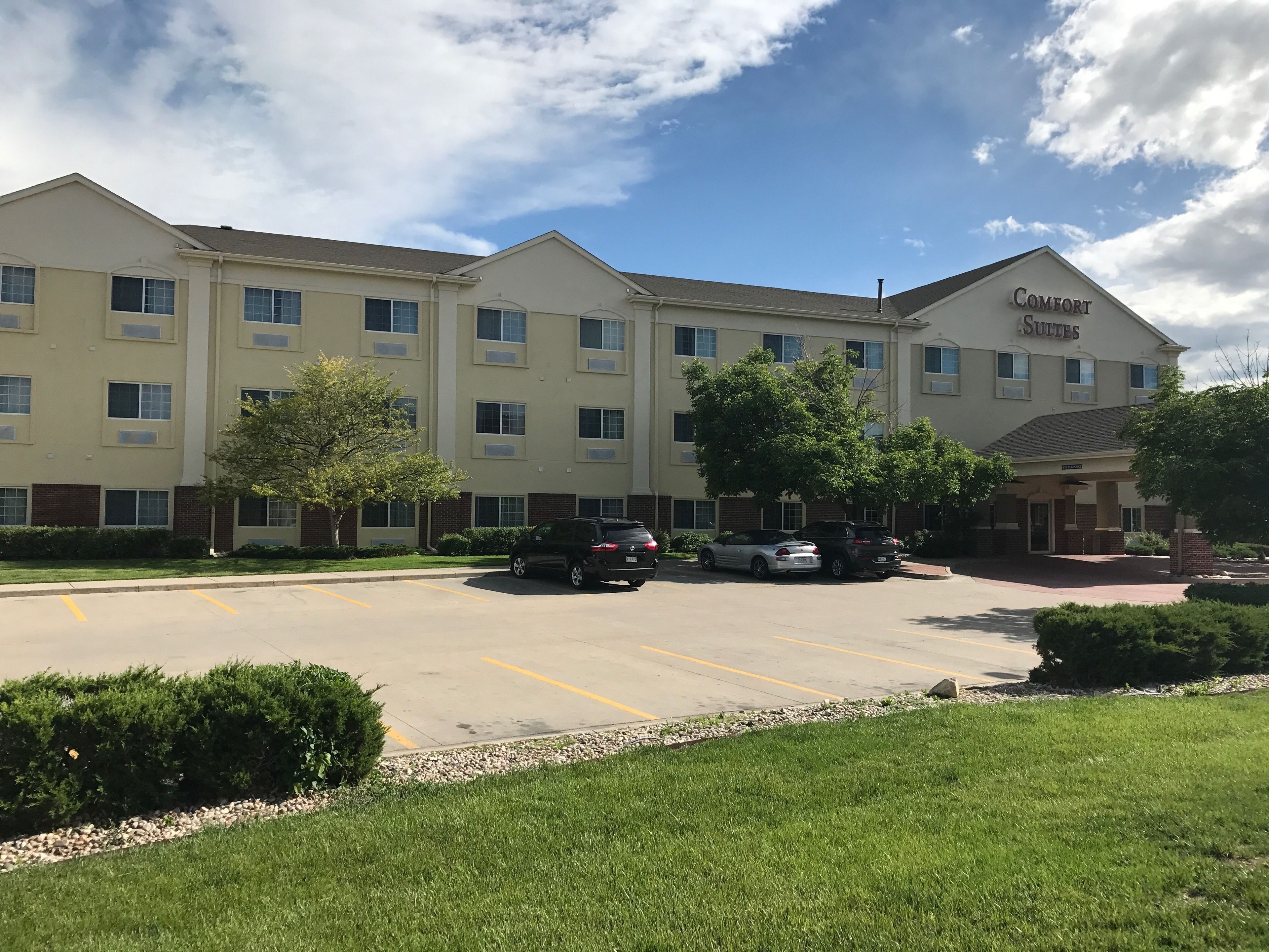 A multi-story hotel with a parking lot, several cars parked, and a well-maintained lawn area.