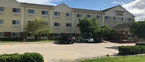 A multi-story hotel with a parking lot, several cars parked, and a well-maintained lawn area.