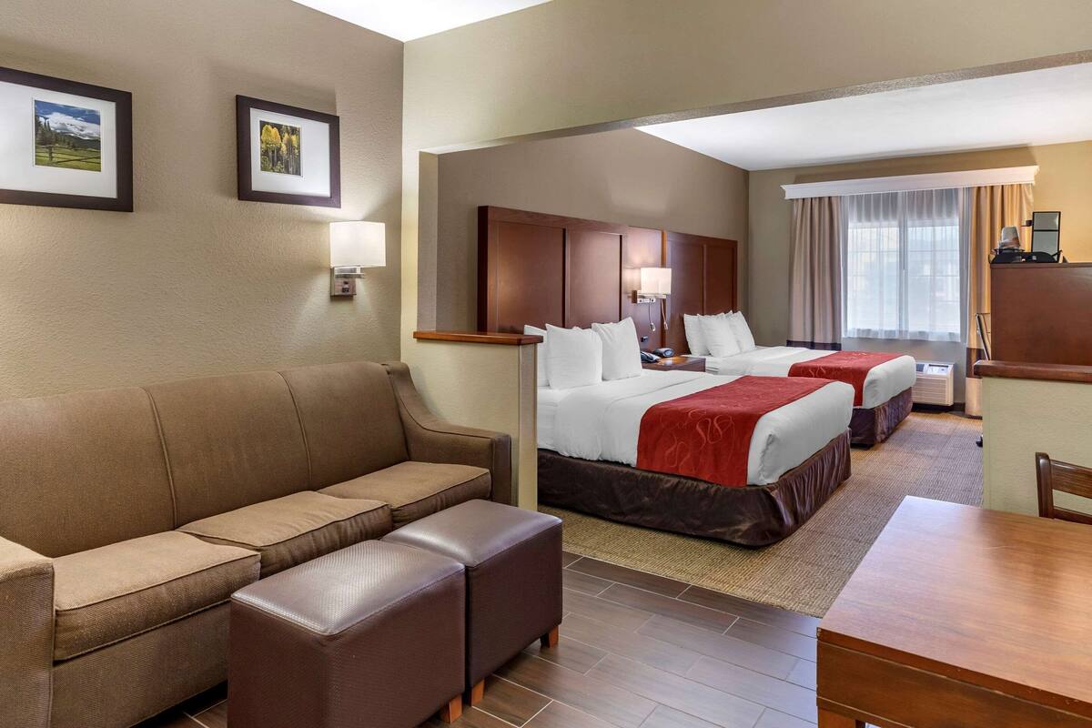 A hotel room with a sofa, two beds, a desk, and a lamp.