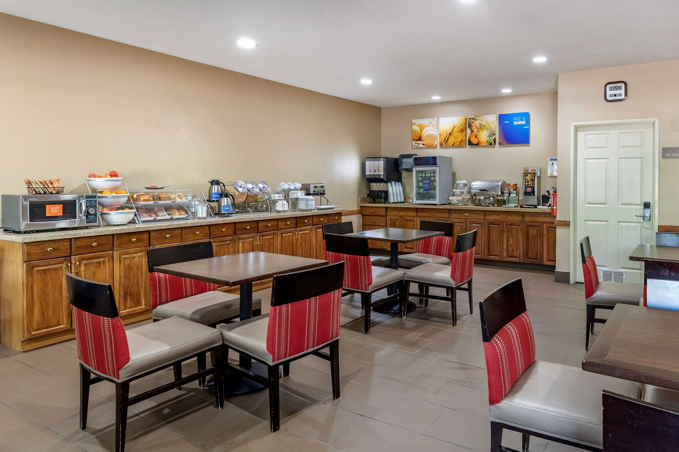 A hotel breakfast area with buffet, coffee machines, and seating.