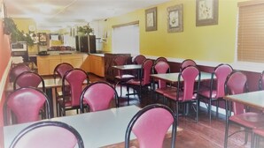 A dining area with tables and chairs, a kitchen area with appliances, and a yellow wall with framed pictures. - Sutton Suites Hotel (SeaTac)