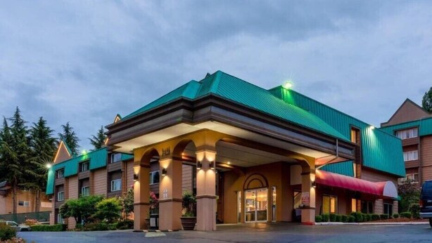 A hotel with a green roof, multiple entry points, and a covered entrance. - Sutton Suites Hotel (SeaTac)
