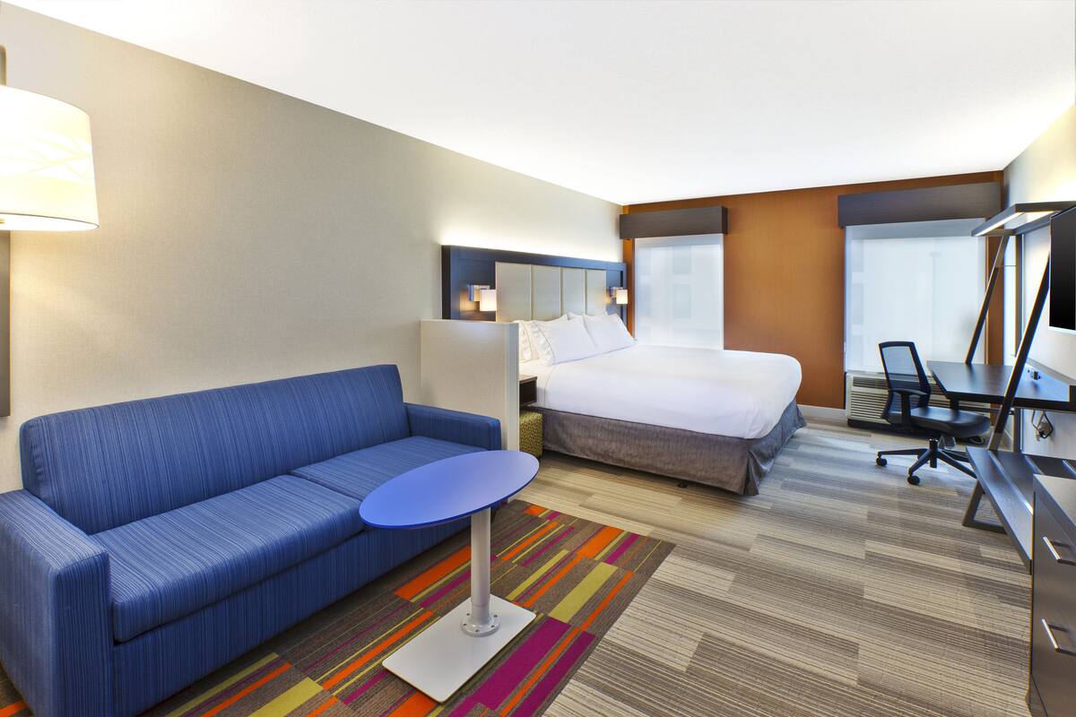 A hotel room with a blue sofa, a bed, a desk, and a TV.