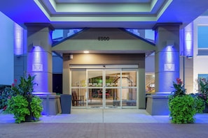 A hotel entrance with a glass door, a number 6500 sign above, and two signs indicating courtesy shuttle pick-up only. - Holiday Inn Express Hotel & Suites Chicago-Midway Airport by IHG (Chicago)