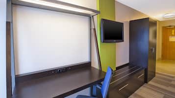 A hotel room with a desk, chair, TV, and a door.