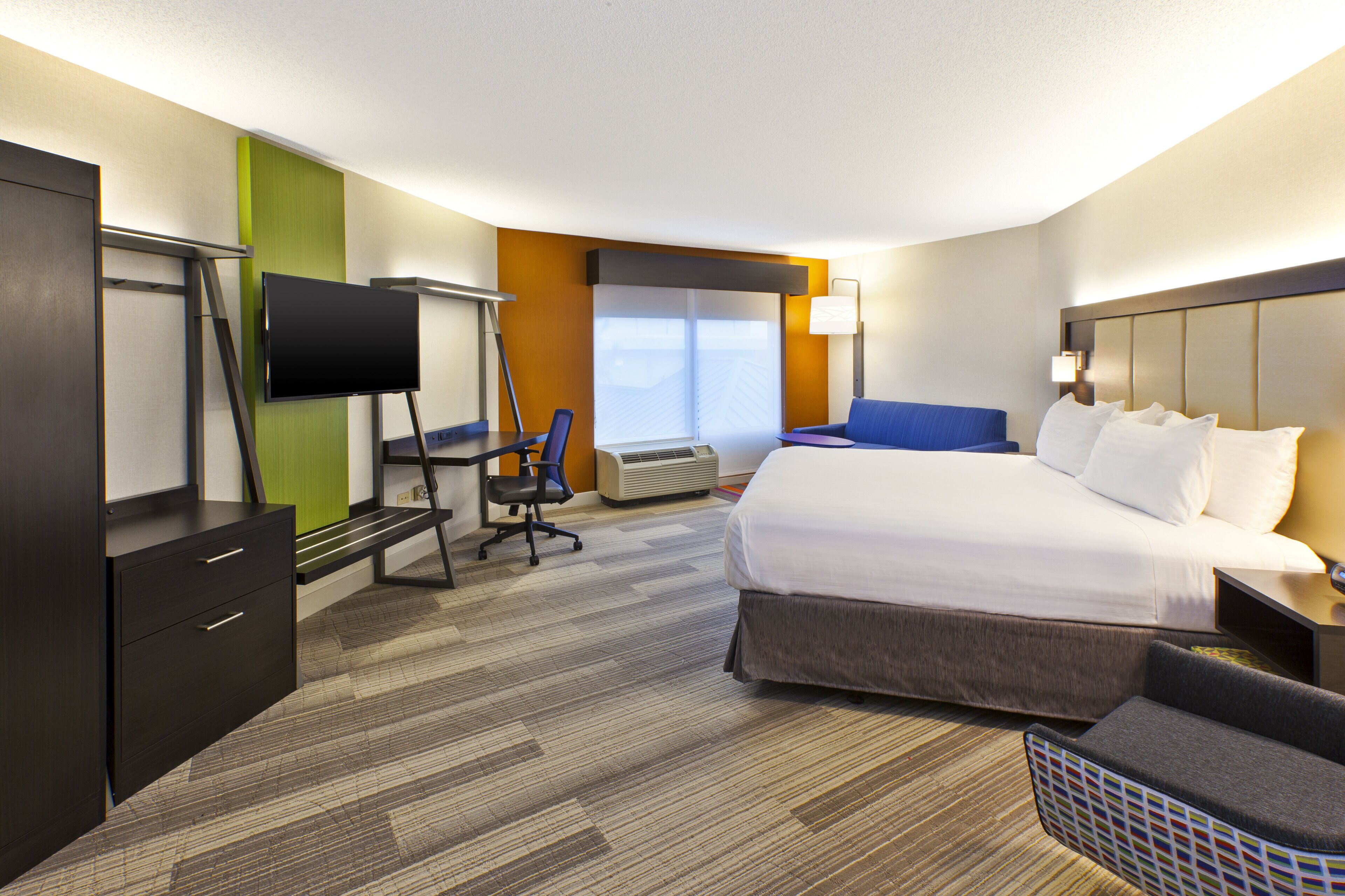 Une chambre d’hôtel comprenant un lit, un bureau avec un téléviseur à écran plat, une chaise, un canapé et une fenêtre donnant sur un paysage agréable.