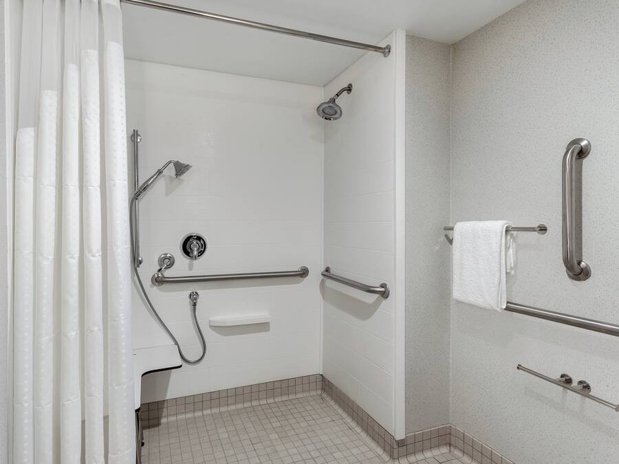 Baño con ducha, barras de apoyo, toallero y un inodoro.