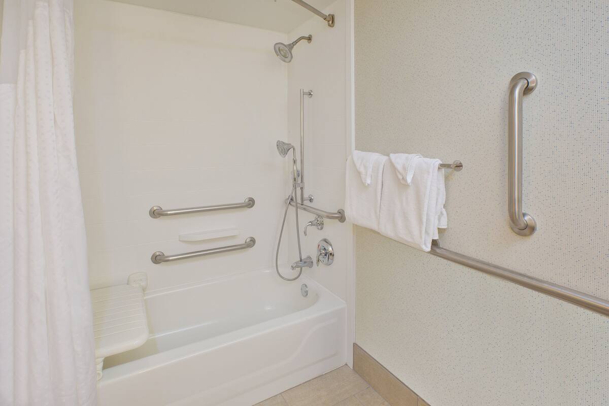 A bathroom with a white bathtub, grab bars, a showerhead, and a towel rack.
