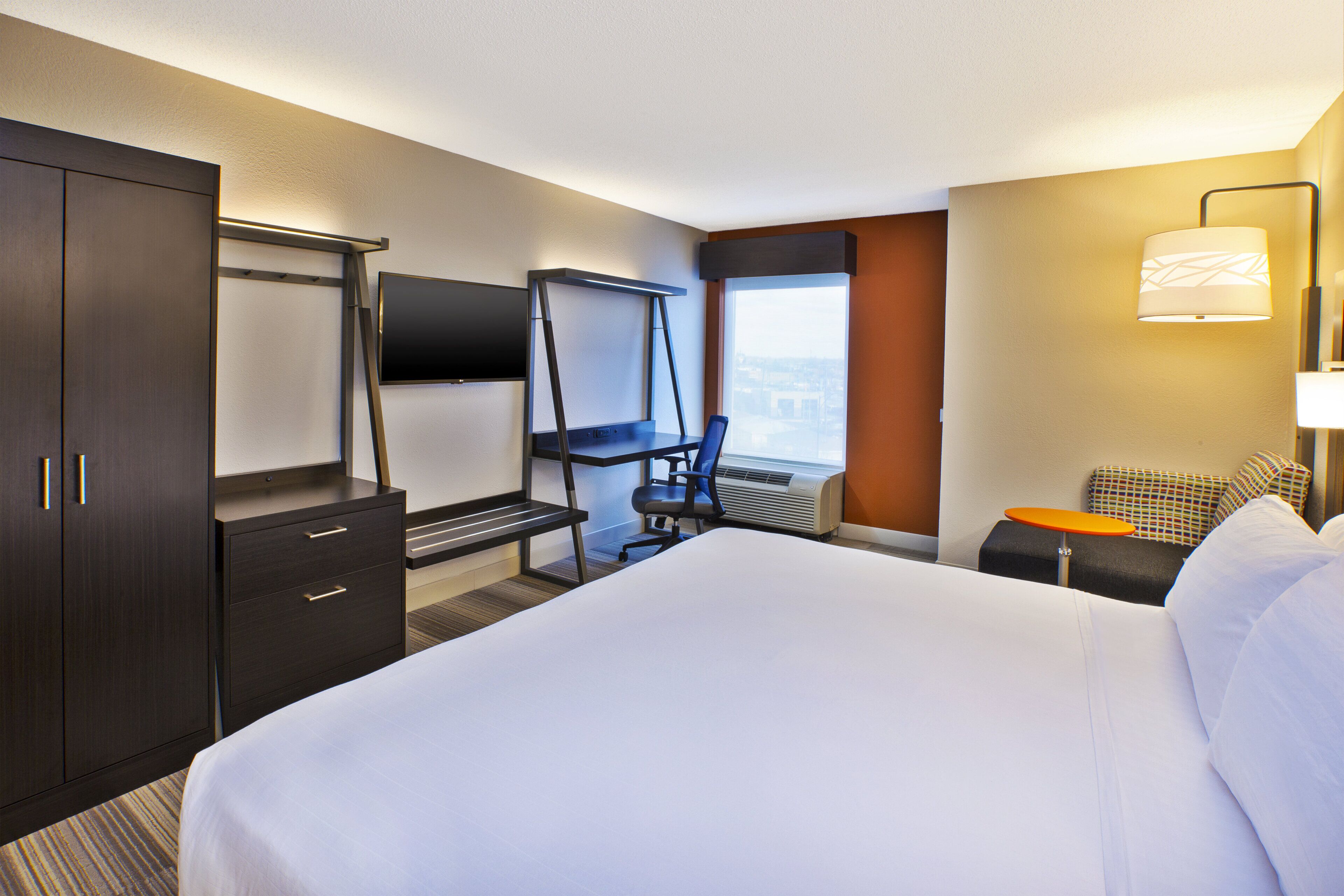 A hotel room with a bed, a desk, a chair, a TV, and a window with a view.