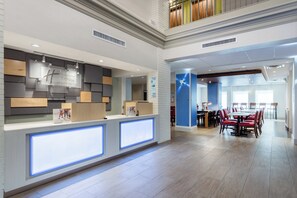 A hotel reception area with a modern design, including a reception desk, a digital display, and a dining area with tables and chairs. - Holiday Inn Express Hotel & Suites Chicago-Midway Airport by IHG (Chicago)