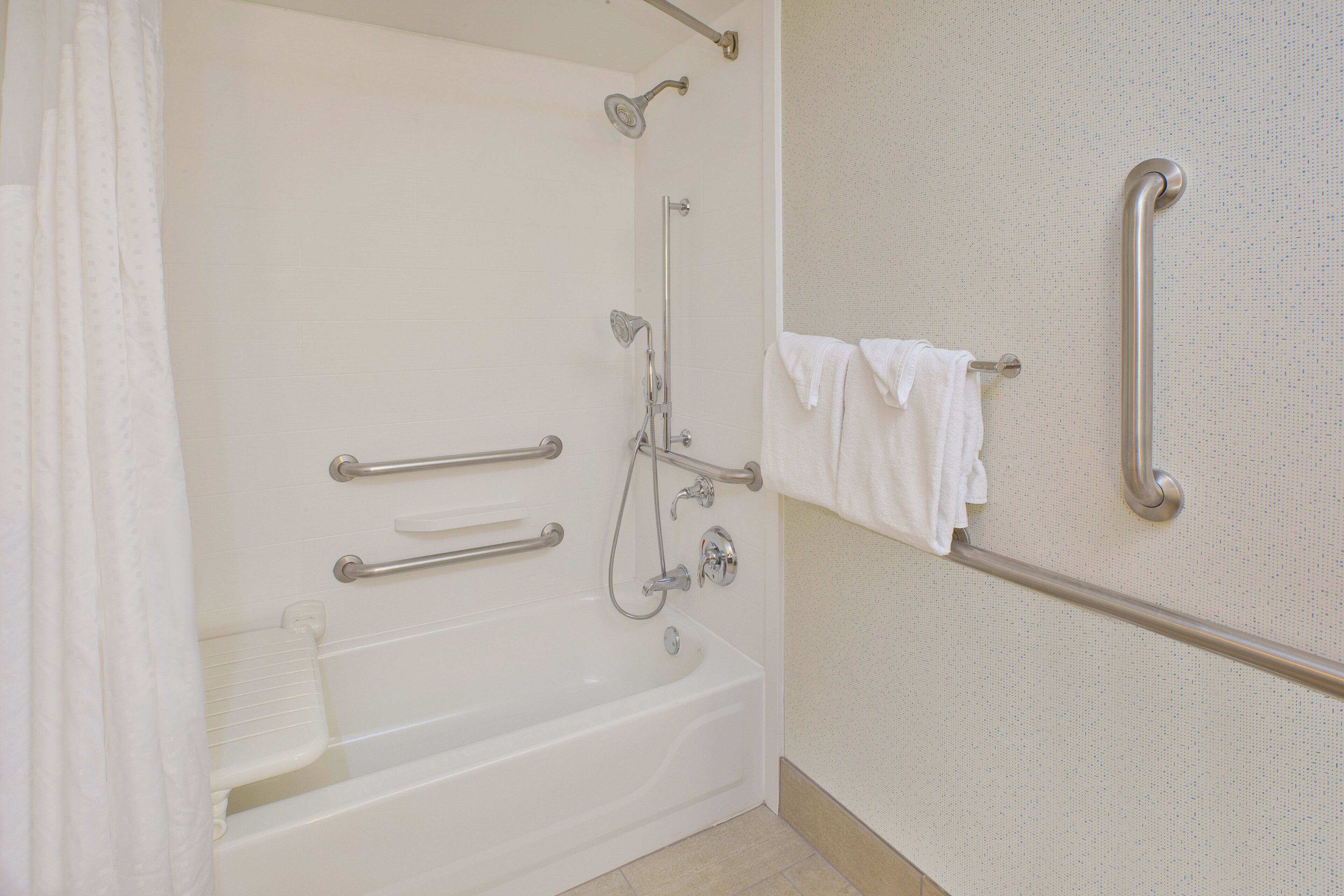 A bathroom with a bathtub, grab bars, a shower, and a towel rack.