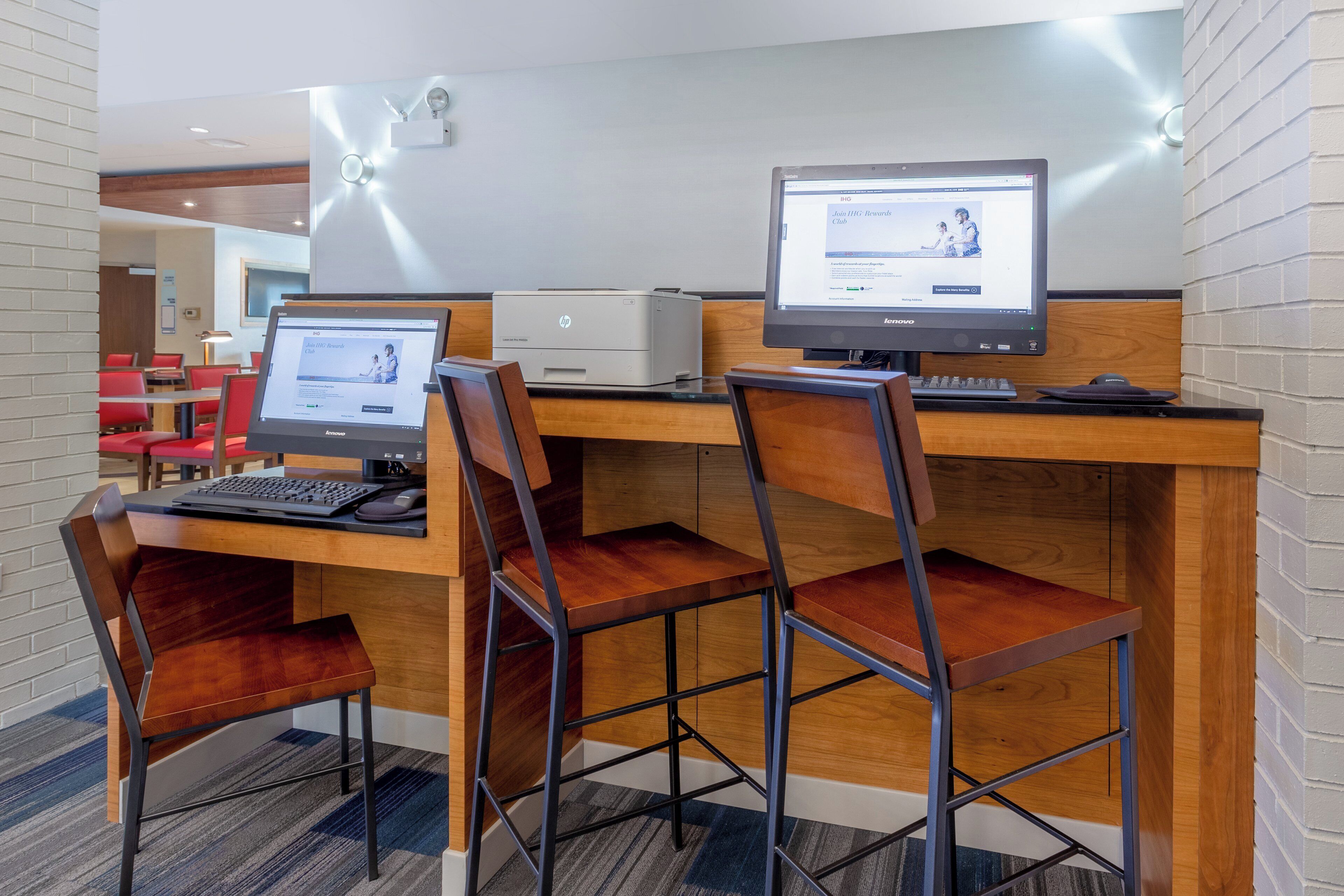 Zona de recepción de hotel con dos estaciones de trabajo de computadora, una impresora y un área de descanso con sillas.