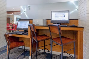 Zona de recepción de hotel con dos estaciones de trabajo de computadora, una impresora y un área de descanso con sillas.