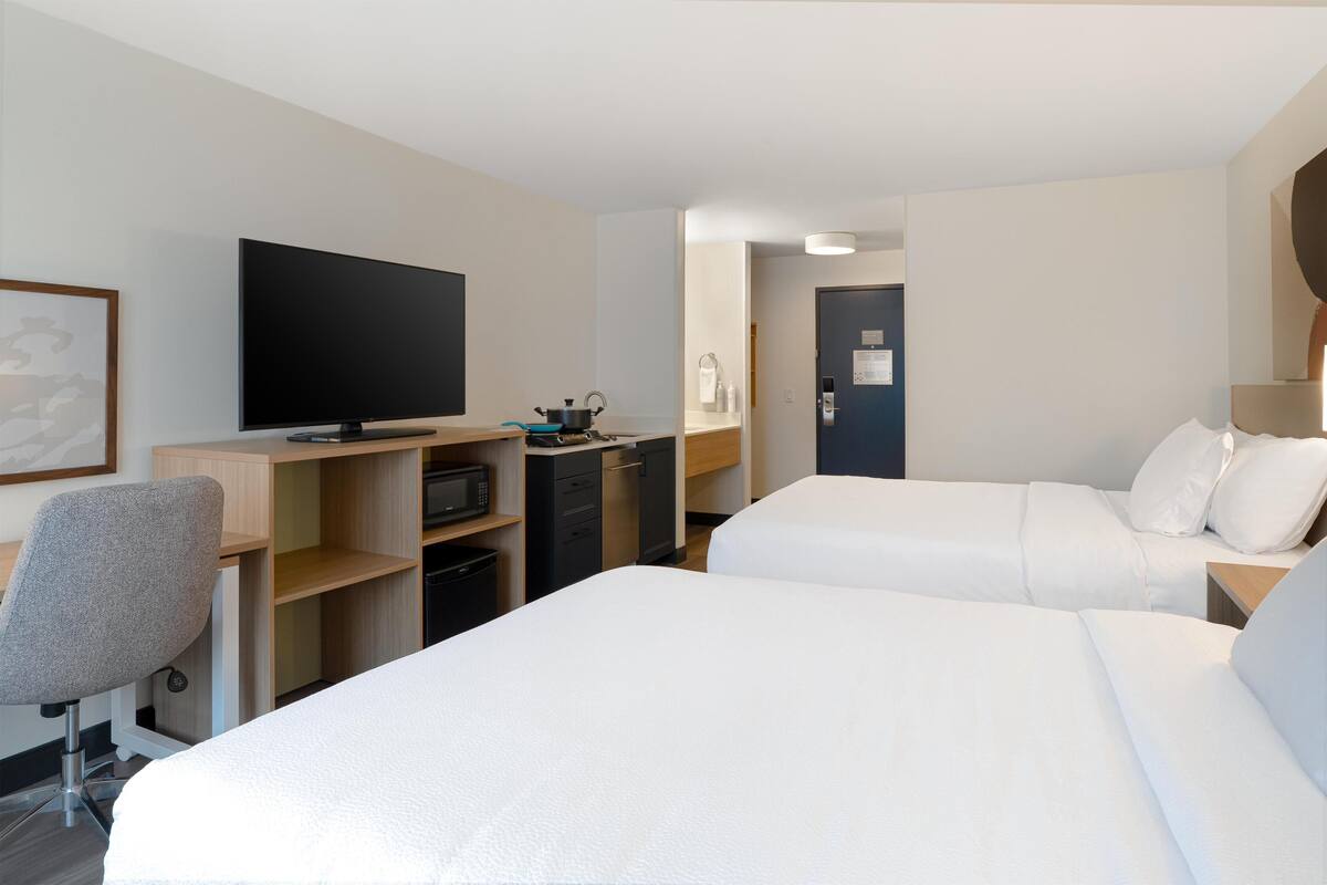 A hotel room with two beds, a desk with a TV, a chair, a microwave, and a door.