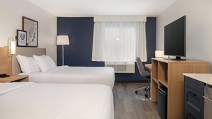 A hotel room with two beds, a desk, a chair, a TV, and a window with curtains.
