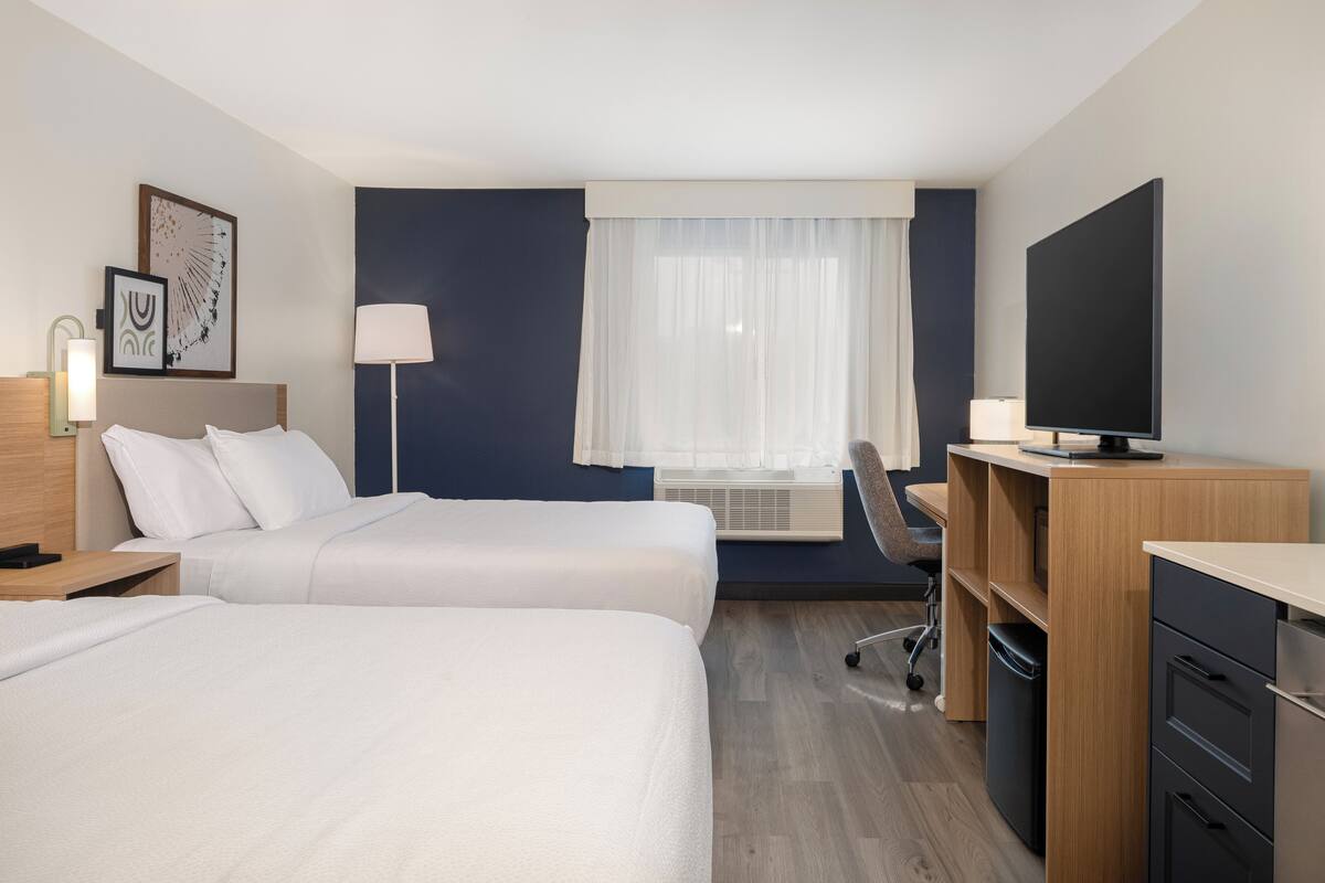 A hotel room with two beds, a desk, a chair, a TV, and a window with curtains.