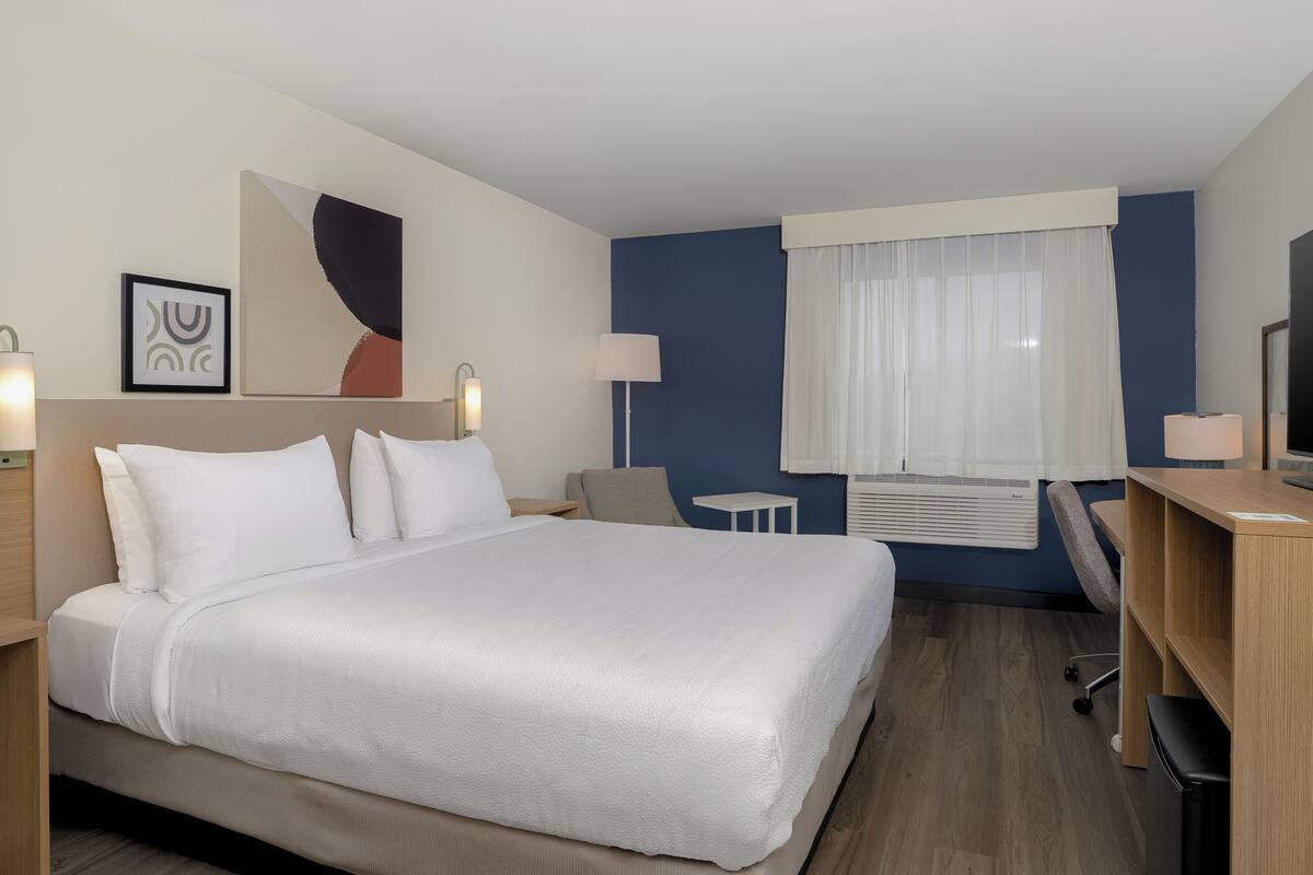 A hotel room with a large bed, a desk, a chair, a small table, and a window with curtains.