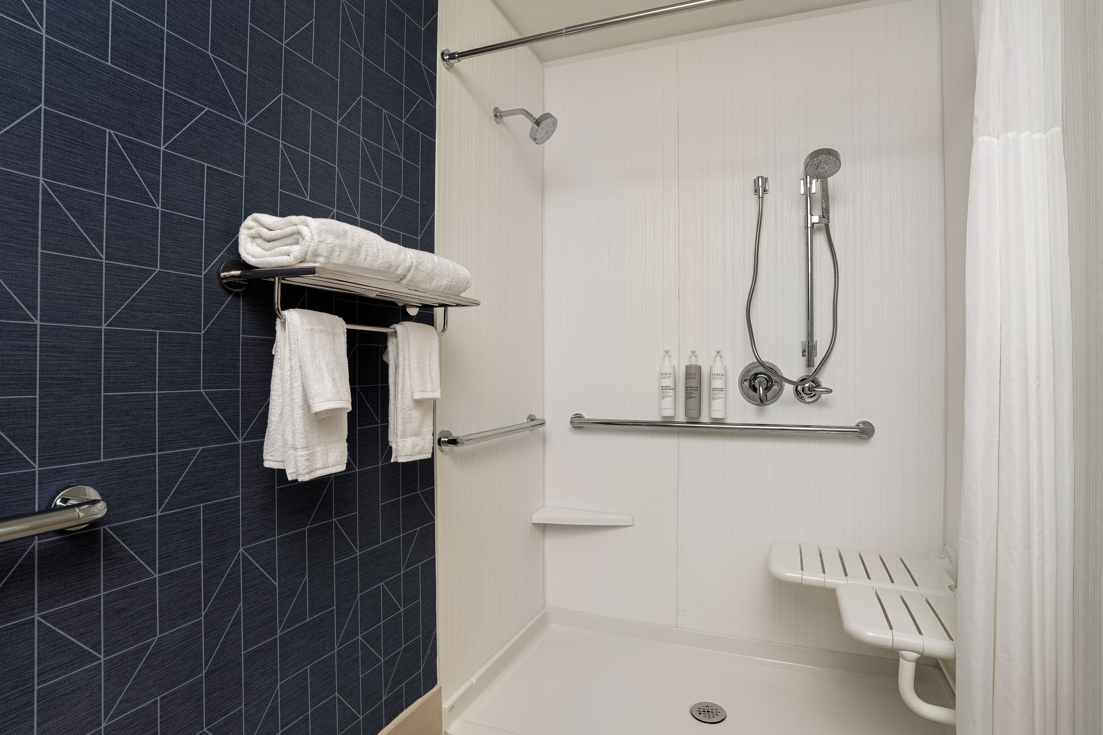 A modern bathroom with a walk-in shower, a white bench, and a towel rack with folded towels.