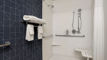 A modern bathroom with a walk-in shower, a white bench, and a towel rack with folded towels.