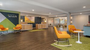 A hotel lobby with orange rocking chairs, a reception desk, and a green carpet.