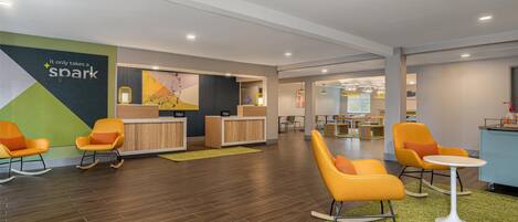 A hotel lobby with orange rocking chairs, a reception desk, and a green carpet.