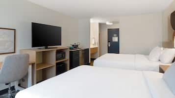 A hotel room with two beds, a desk with a television, a chair, and a kitchenette.