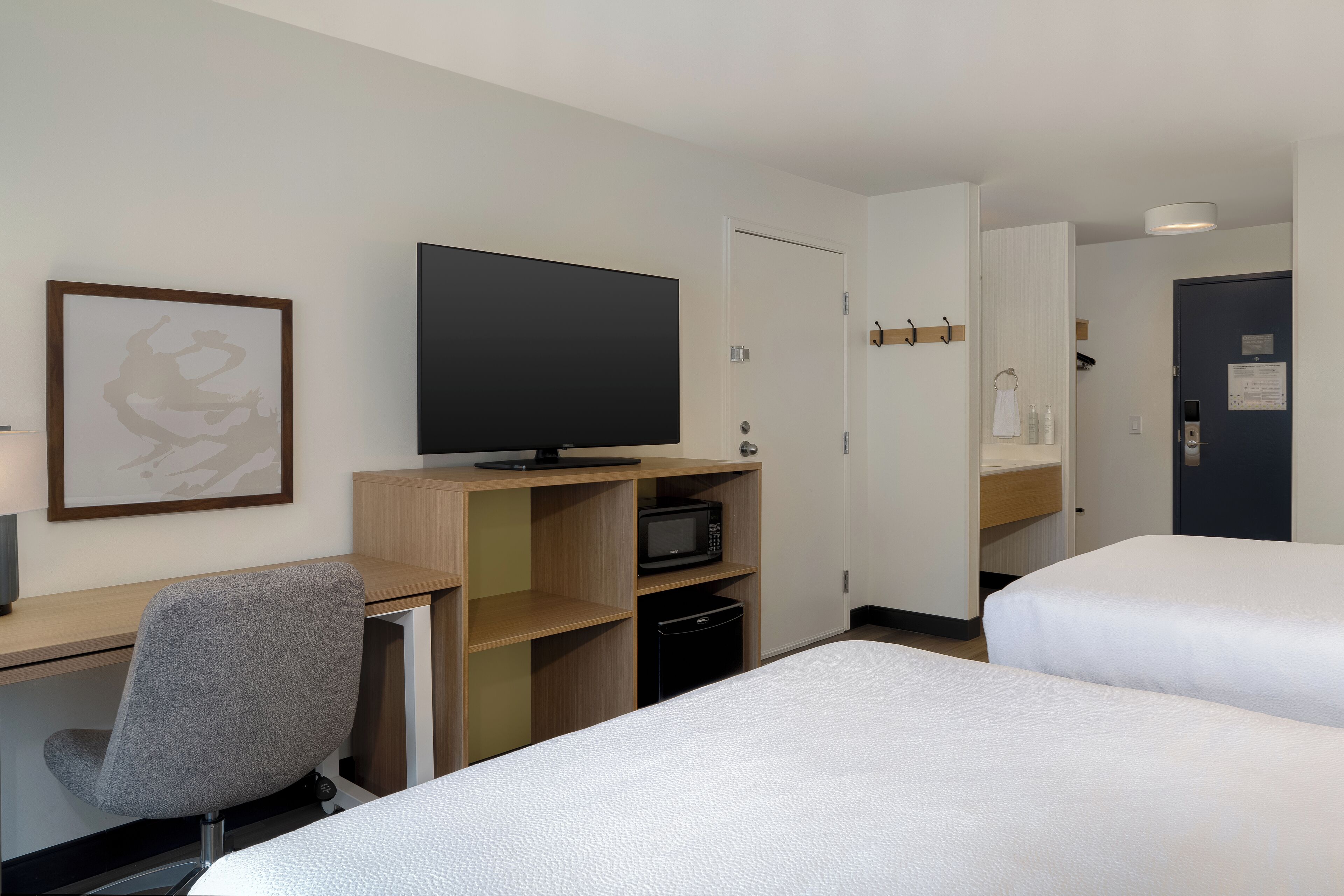 Een hotelkamer met een bed, een bureau met stoel, een televisie en een magnetron.