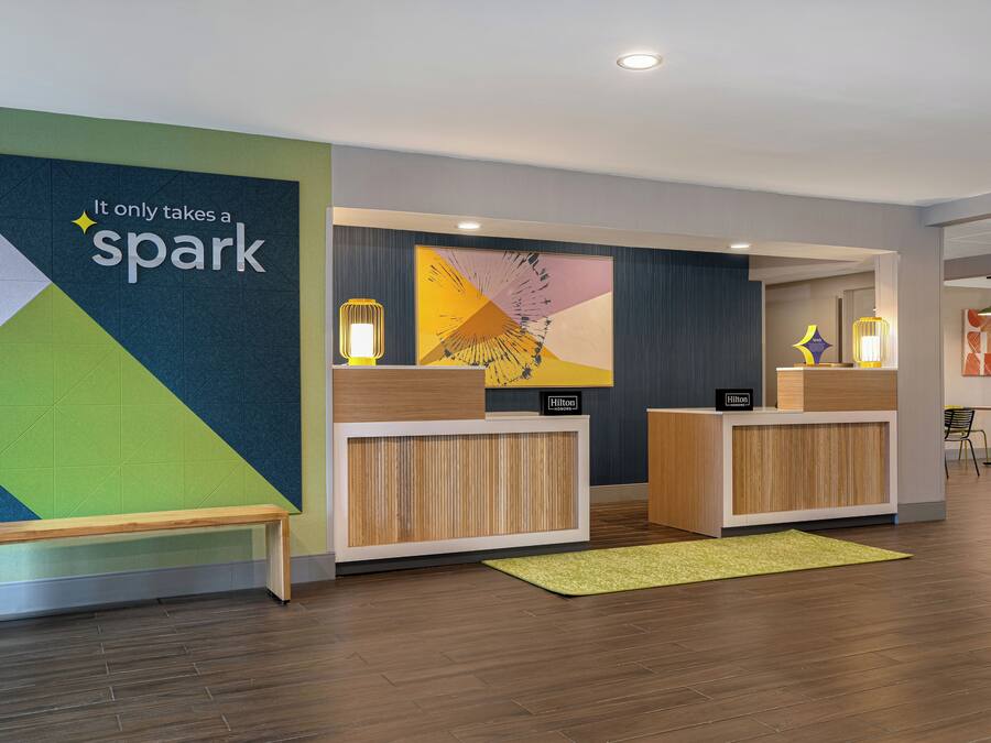 Un'area reception dal design moderno, con una parete caratterizzata da un motivo geometrico e la scritta 'It only takes a spark'.