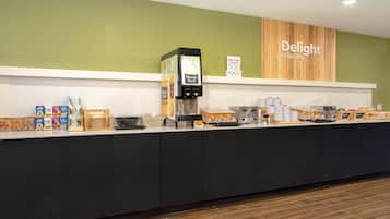Una barra de desayuno con una máquina de café, un letrero que dice 'Delight in the day' y diversas opciones de comida.