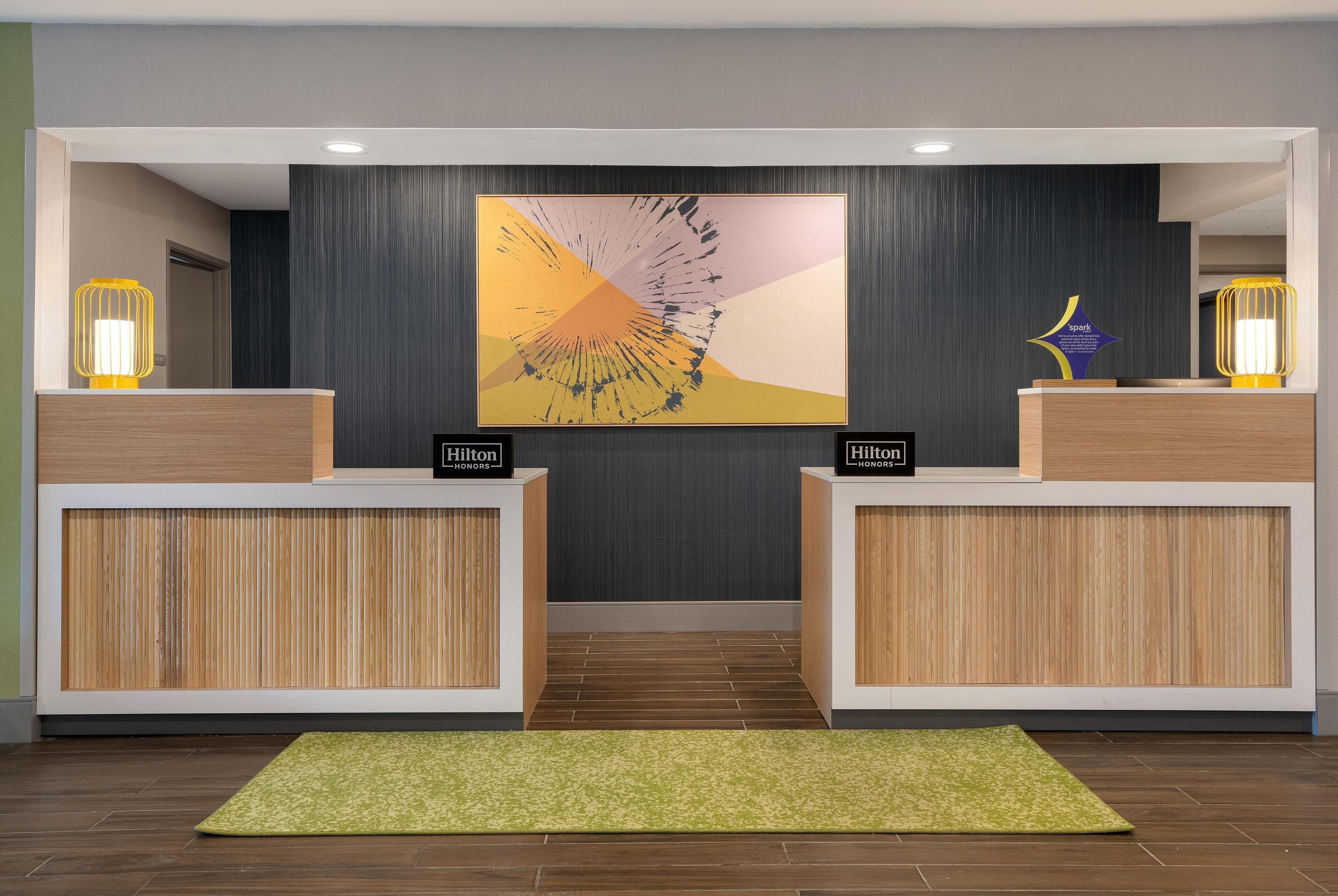 A reception area with a modern design, featuring a large abstract painting, two reception desks, and a green carpet.