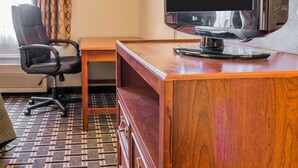 A hotel room with a wooden desk, a black office chair, a flat-screen TV, and a lamp. - Quality Inn Grand Rapids North (Grand Rapids)