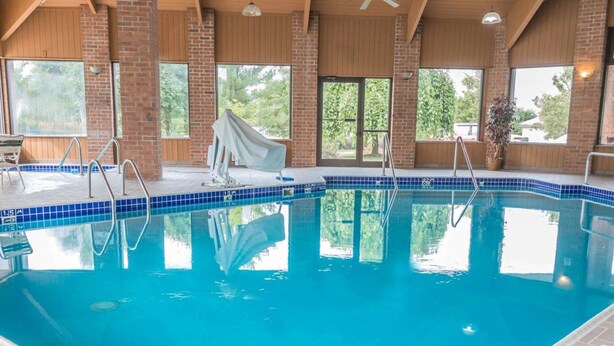 An indoor swimming pool with clear blue water, a diving board, and a bench. - Quality Inn Grand Rapids North (Grand Rapids)