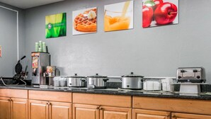 A kitchen with wooden cabinets, a countertop with various appliances, and wall art depicting food items. - Quality Inn Grand Rapids North (Grand Rapids)