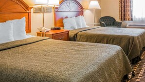 A hotel room with two beds, a wooden headboard, a nightstand with a lamp, a chair, and a window with curtains. - Quality Inn Grand Rapids North (Grand Rapids)
