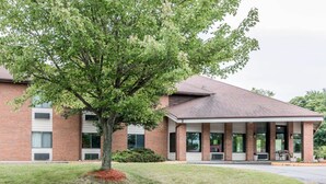 A two-story brick building with a covered front porch and a large tree in front. - Quality Inn Grand Rapids North (Grand Rapids)