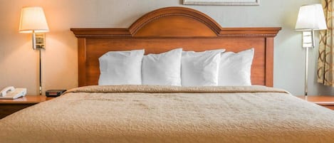 Habitación de hotel con cabecera de madera, cama con ropa de cama blanca, mesita de noche con lámpara y un cuadro en la pared.
