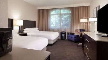 A hotel room with two beds, a desk, a TV, a lamp, and a window with curtains.