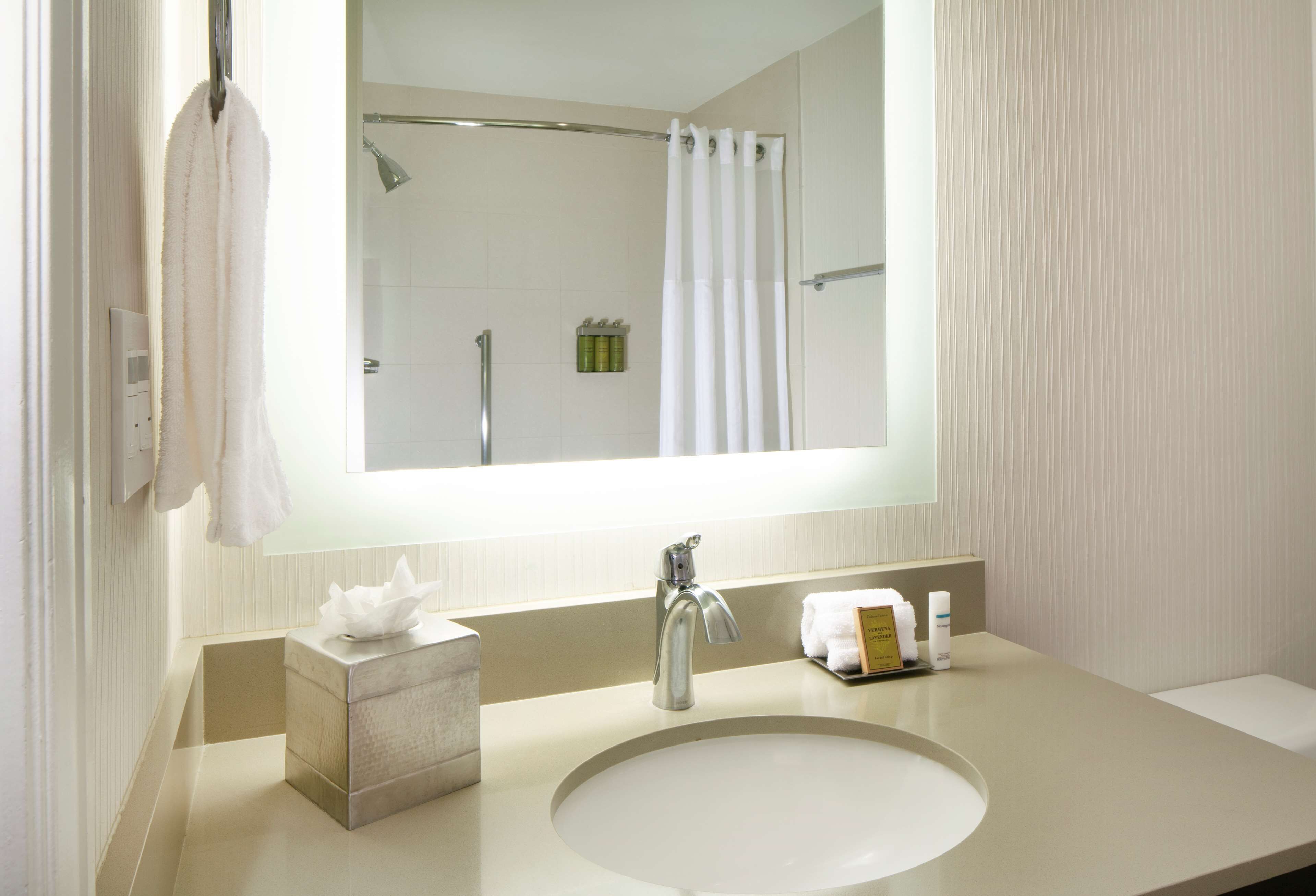A bathroom with a large mirror, a sink, a towel rack, and a shower area.