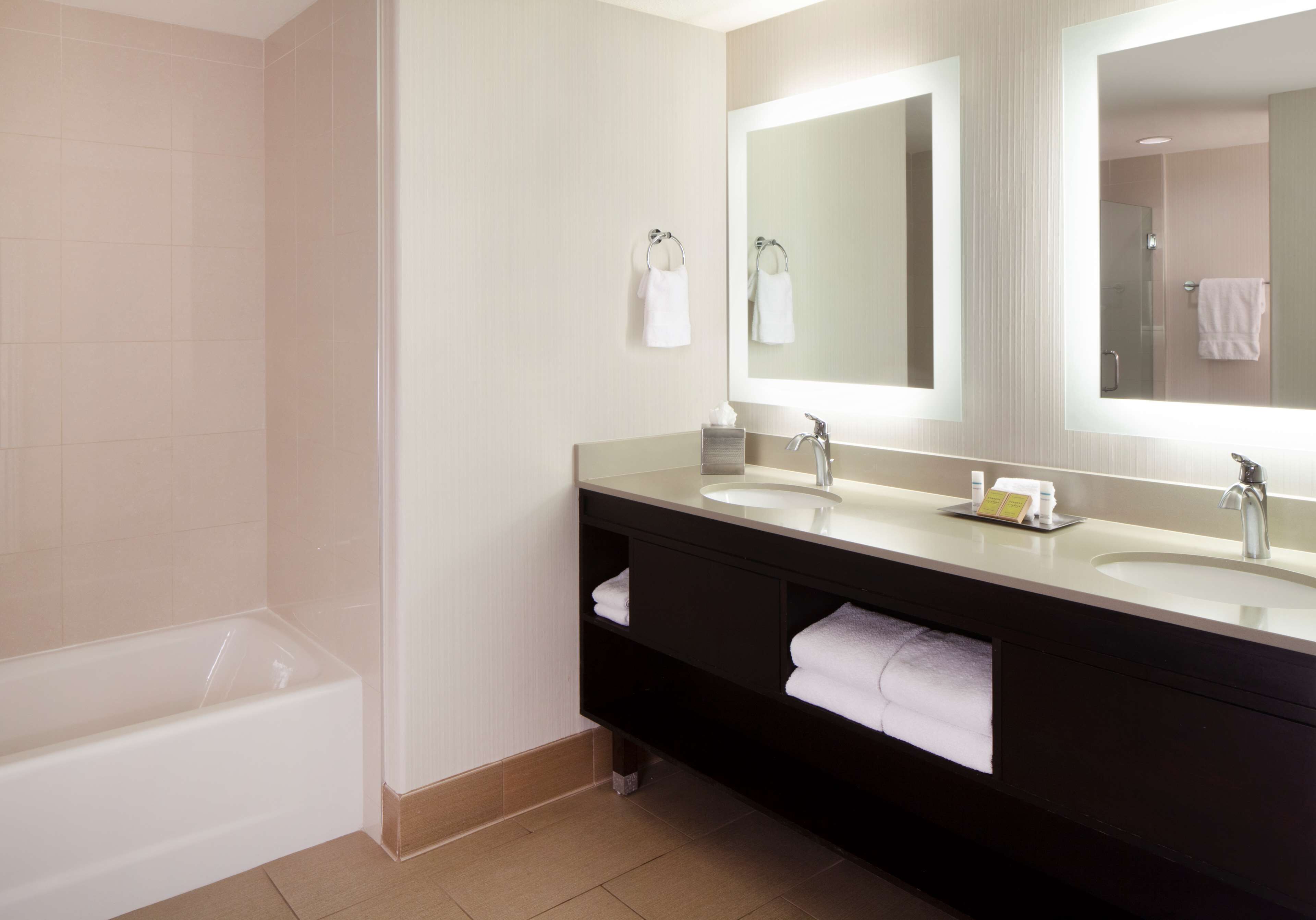 A modern bathroom with a bathtub, two sinks, and a large mirror.