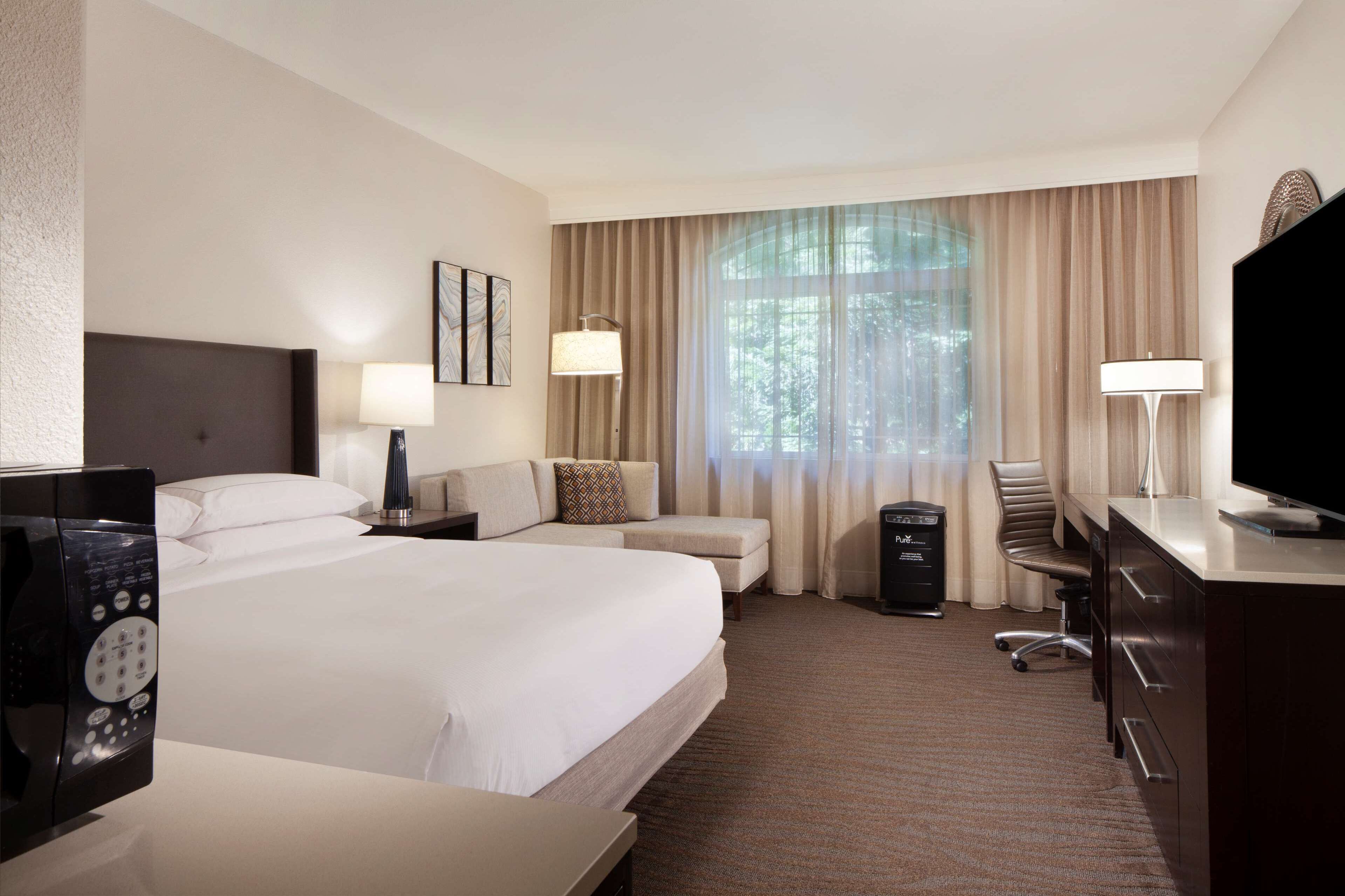 A hotel room with a large bed, two bedside tables, a desk with a chair, a television, and a window with curtains.