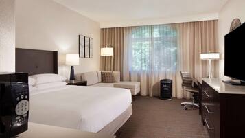 A hotel room with a large bed, two bedside tables, a desk with a chair, a television, and a window with curtains.