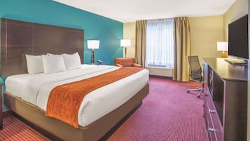 A hotel room with a large bed, two bedside lamps, a desk with a TV, and a window with curtains.